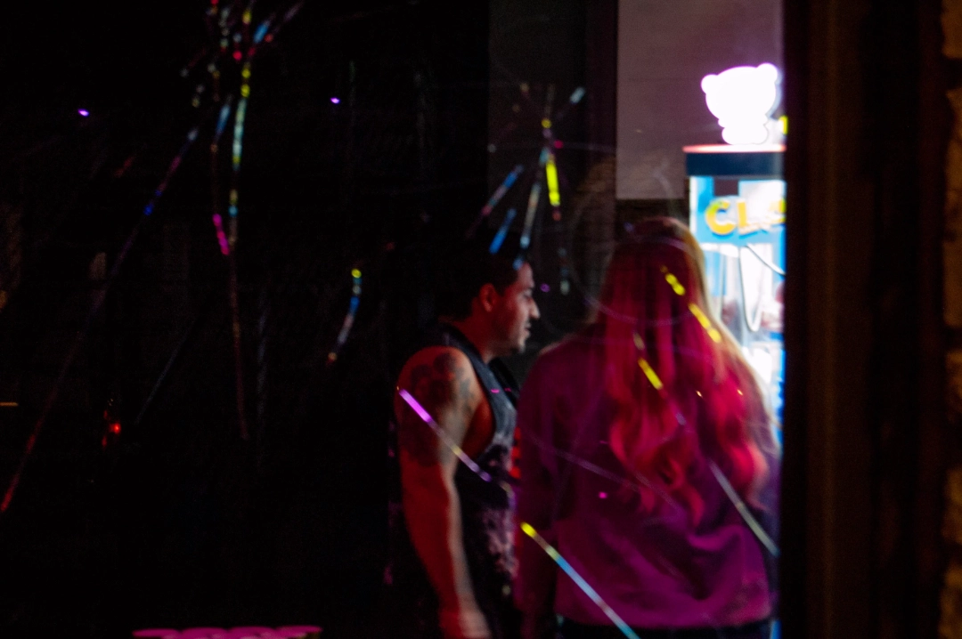 A couple at a claw machine, seen through a cracked window.