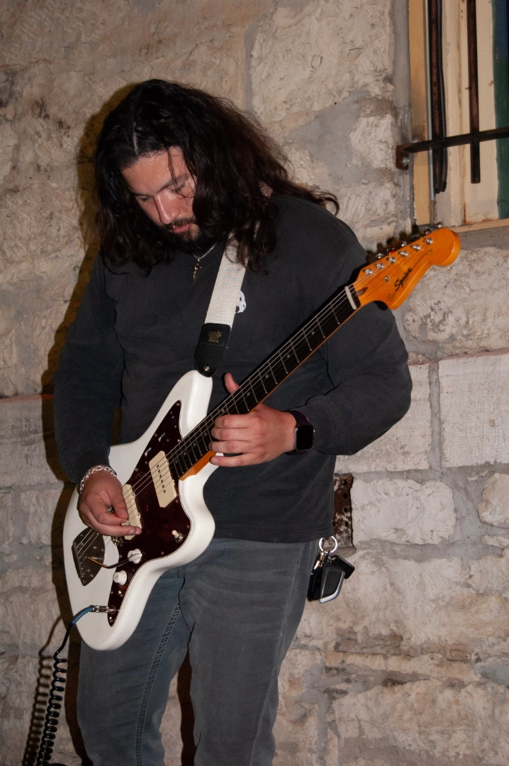 A man playing a white electric guitar outside.